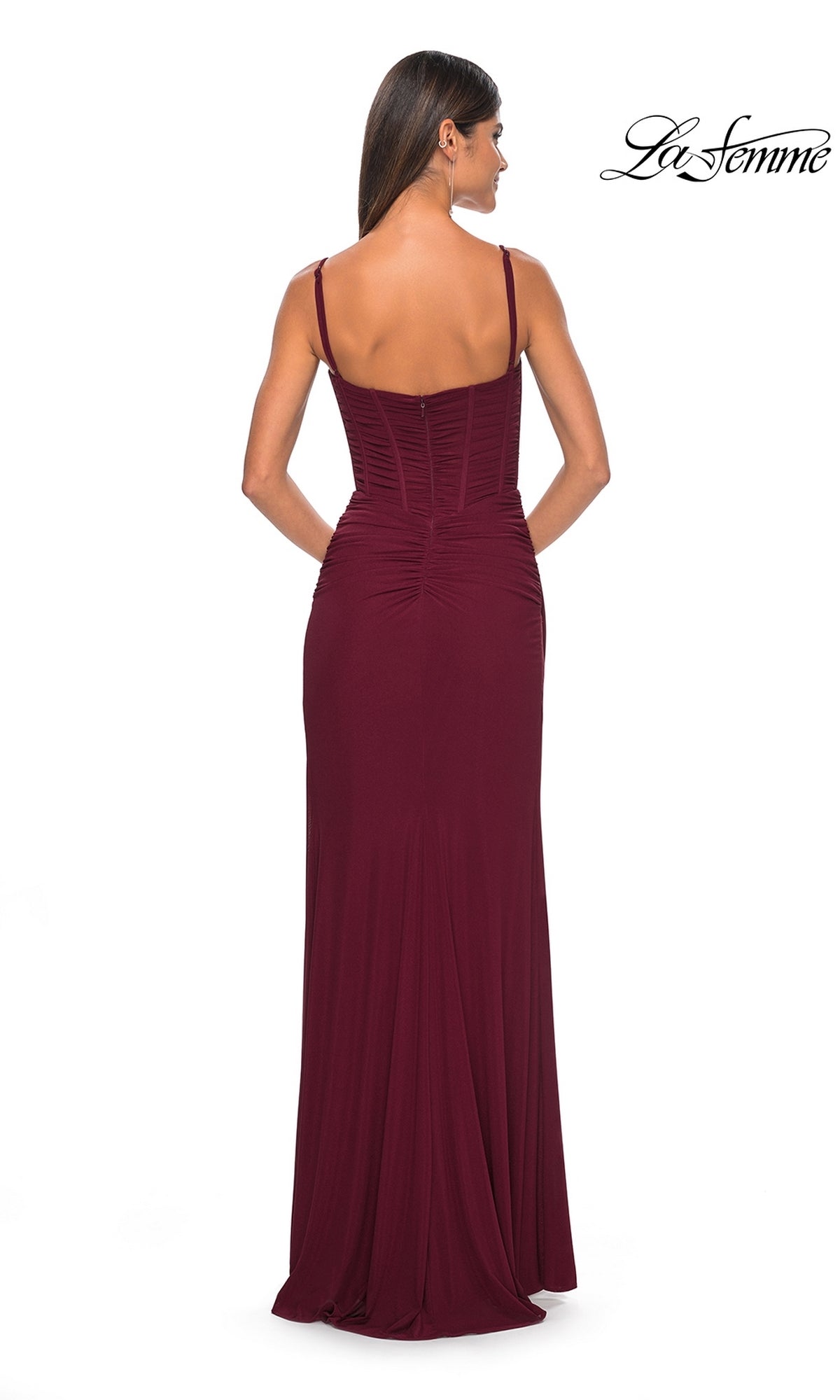 A woman faces away, wearing a sleeveless, floor-length burgundy La Femme Faux-Wrap Long Corset Prom Dress 32239 with thin straps and subtle ruching, against a white background.
